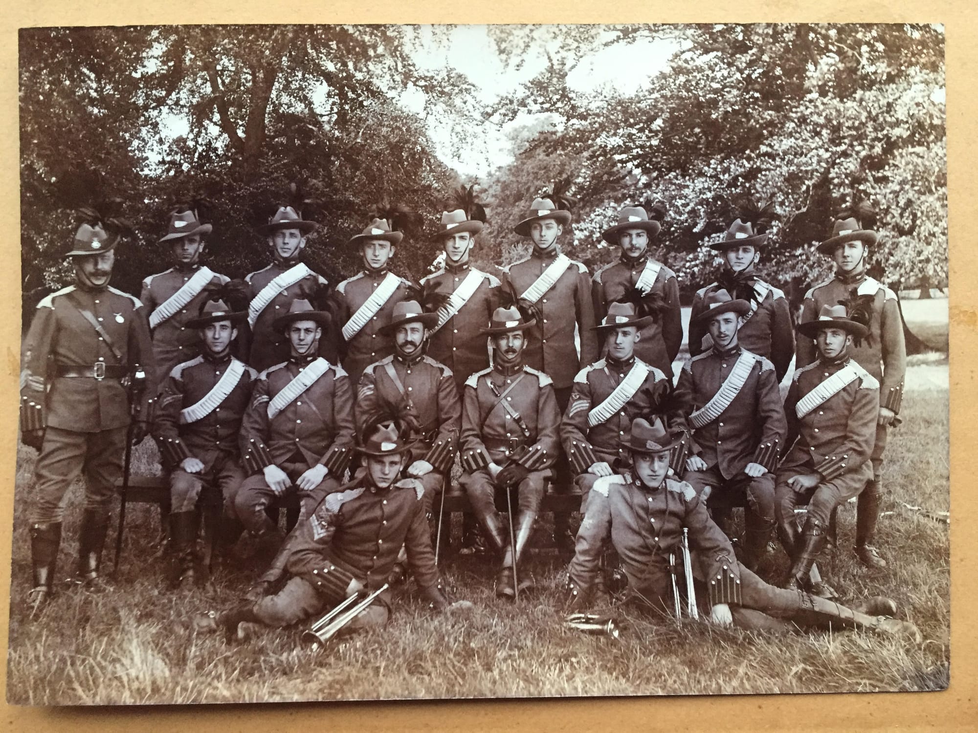 Full Dress uniform of a Regimental Quartermaster Sergeant (standing far left), NCOs and Other Ranks of the 3rd (New Zealand) Troop of ‘D’ (South African) Squadron of the King’s Colonials Imperial Yeomanry circa 1905-06. The Regimental Quarter Master Sergeant is wearing a Second Pattern Regimental headdress badge and the Other Ranks are wearing New Zealand headdress and matching collar badges. Squadron Quarter Master Serjeant MacIntosh is the NCO with the mustache seated left of the Officer in the centre of the middle row (The Officer in command of 'C' Troop in 1902 was Captain R. S. Vaile and it could be him but he looks to be wearing a single crown shoulder rank of a Major). The two trumpeters seated in the front row are both wearing cloth trumpeter arm badges on the left upper sleeve (shown in Denis Edwards and David Langley: British Army Proficiency Badges. The Sherwood Press, Nottingham, 1984 as 156A). The Corporal Trumpeter on the left is wearing his cloth trumpeter arm badge above his two rank chevrons. The Senior NCOs are carrying swords and the Other Ranks are wearing Boer War period, 50-round Mills equipment webbing bandoliers (David Stewart collection).