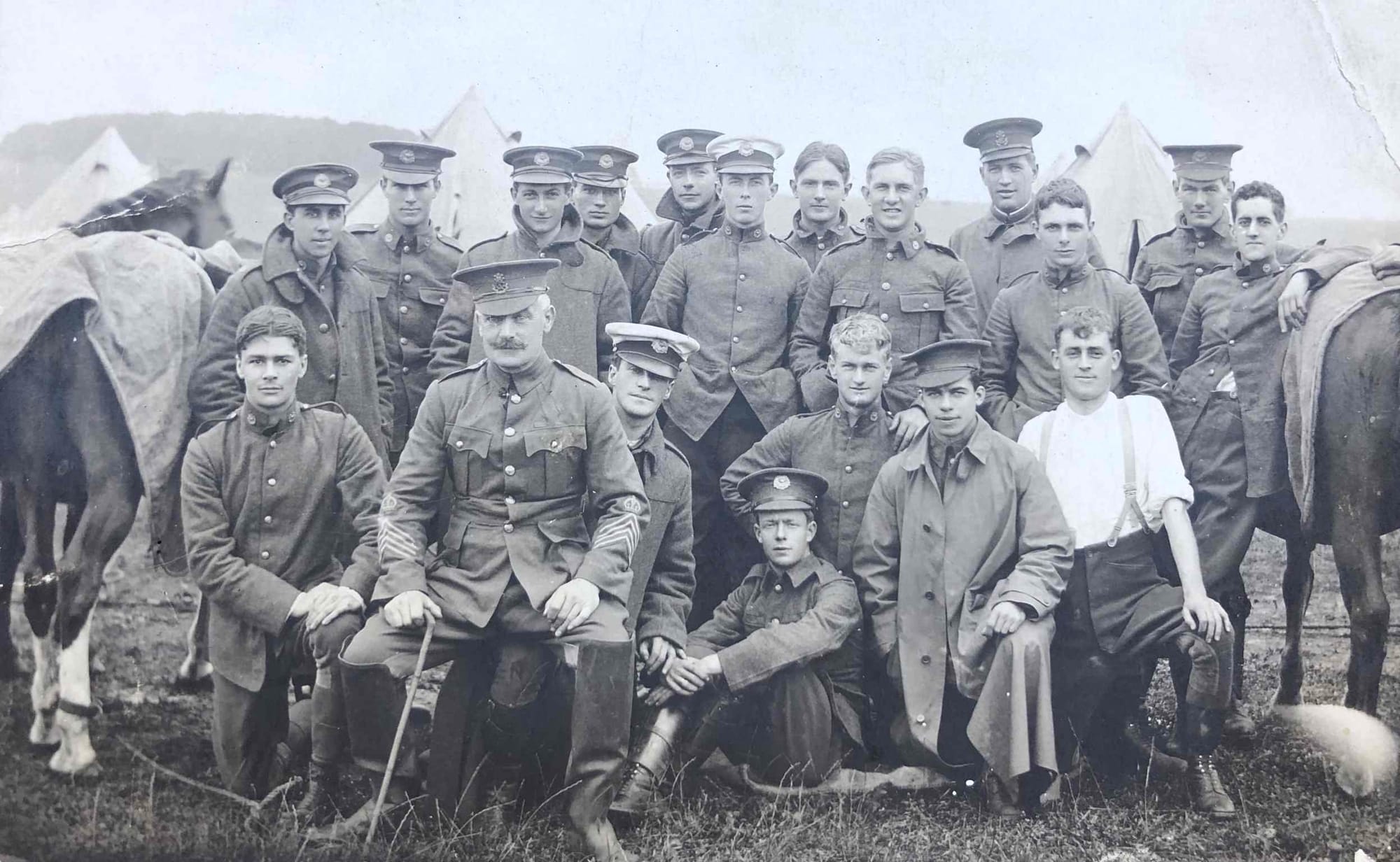 A group photograph at annual camp circa 1905-10 of 'D' Squadron (British African) of the King's Colonials wearing Service Dress.  The Squadron Quartermaster Sergeant is wearing his crown above the four Quartermaster chevrons on both lower sleeves. He wears the Regimental badge in his cap unlike the majority of the Other Ranks wearing Squadron headdress badges and Squadron collar badges.