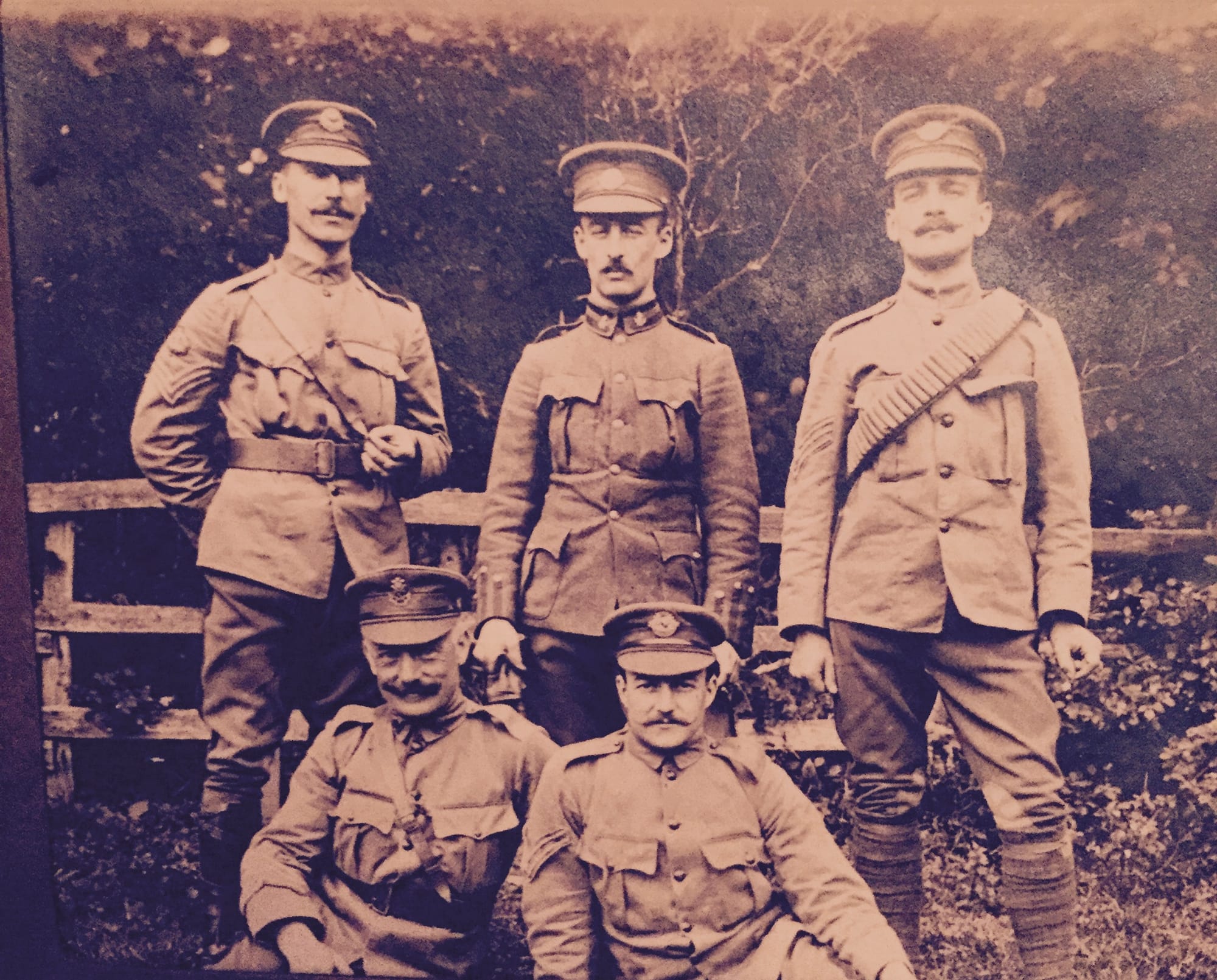 Regimental Quartermaster Sergeant (left, front row) wearing a Second Pattern Regimental headdress badge, the Squadron Sergeant Major (left, rear row) wearing the ‘D’ Squadron (British African) headdress badge, Sergeant MacIntosh (right, rear row) and a Corporal ( right, front row) of the 3rd Troop (New Zealand) of ‘D’ Squadron (British African) wearing Australasian headdress badges of the King’s Colonials Imperial Yeomanry wearing standard British Army Service Dress tunics, overalls and the first pattern khaki forage caps circa 1904. The Officer of the 3rd Troop, ‘D’ Squadron (British African) (middle, rear row) is wearing Undress uniform with the Australasian headdress badge. Sergeant MacIntosh is equipped with a Boer War period, 50-round Mills equipment webbing bandolier and puttees.