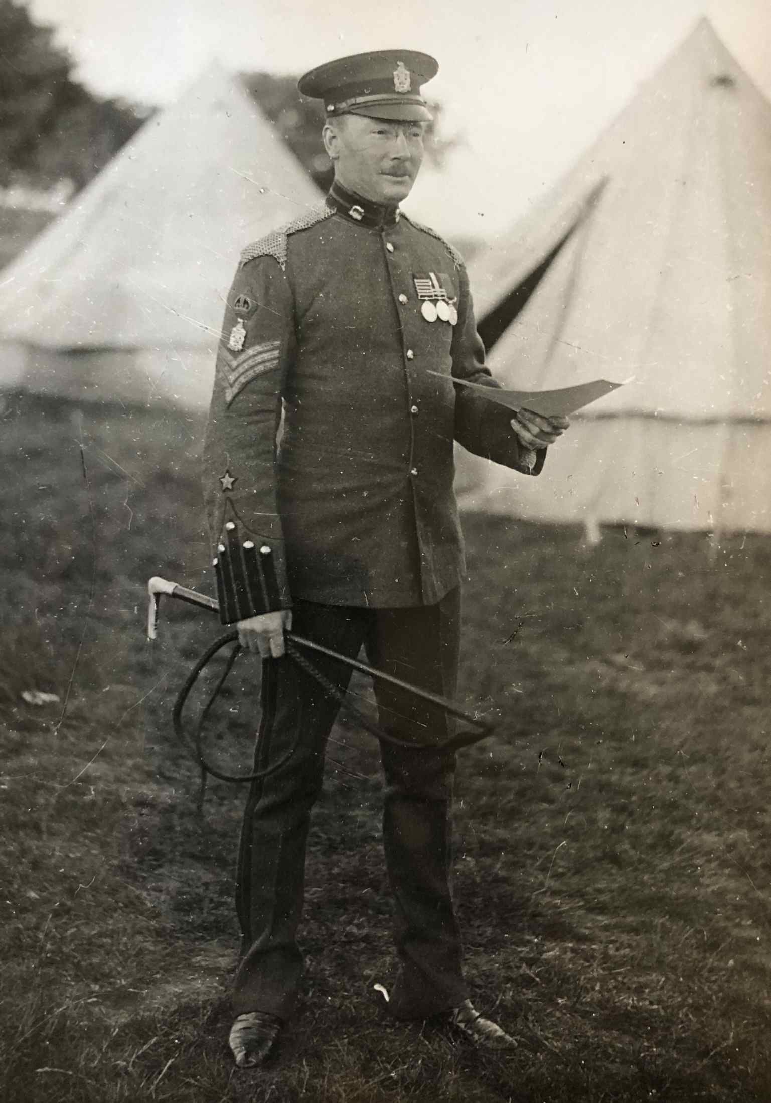 Photograph of Squadron Sergeant Major Harry Campbell Calvert, King Edward’s Horse in Undress uniform with a forage cap with a tan leather peak circa 1912. He is wearing ‘A’ Squadron (British Asian) collar badges, a King Edward’s Horse headdress badge and a bullion crown denoting his rank above a further King Edward’s Horse badge worn above his rank chevrons. He is wearing a five bar Queen's South Africa medal, a two bar King's South Africa medal and an Army Long Service and Good Conduct medal which was awarded to Regular Force non-commissioned officers and men who had completed eighteen years of irreproachable service. He is wearing a single Volunteer's Efficiency star above his right cuff denoting that he has attended a sufficient number of drills, parades and an annual camp over four years.