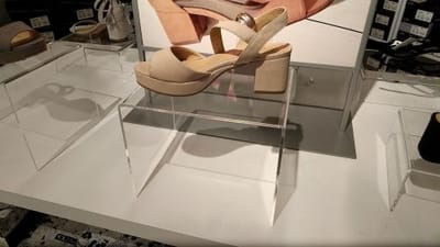 Clear acrylic riser display showcasing a stylish beige high-heeled shoe, designed for elegant product presentation in retail settings.