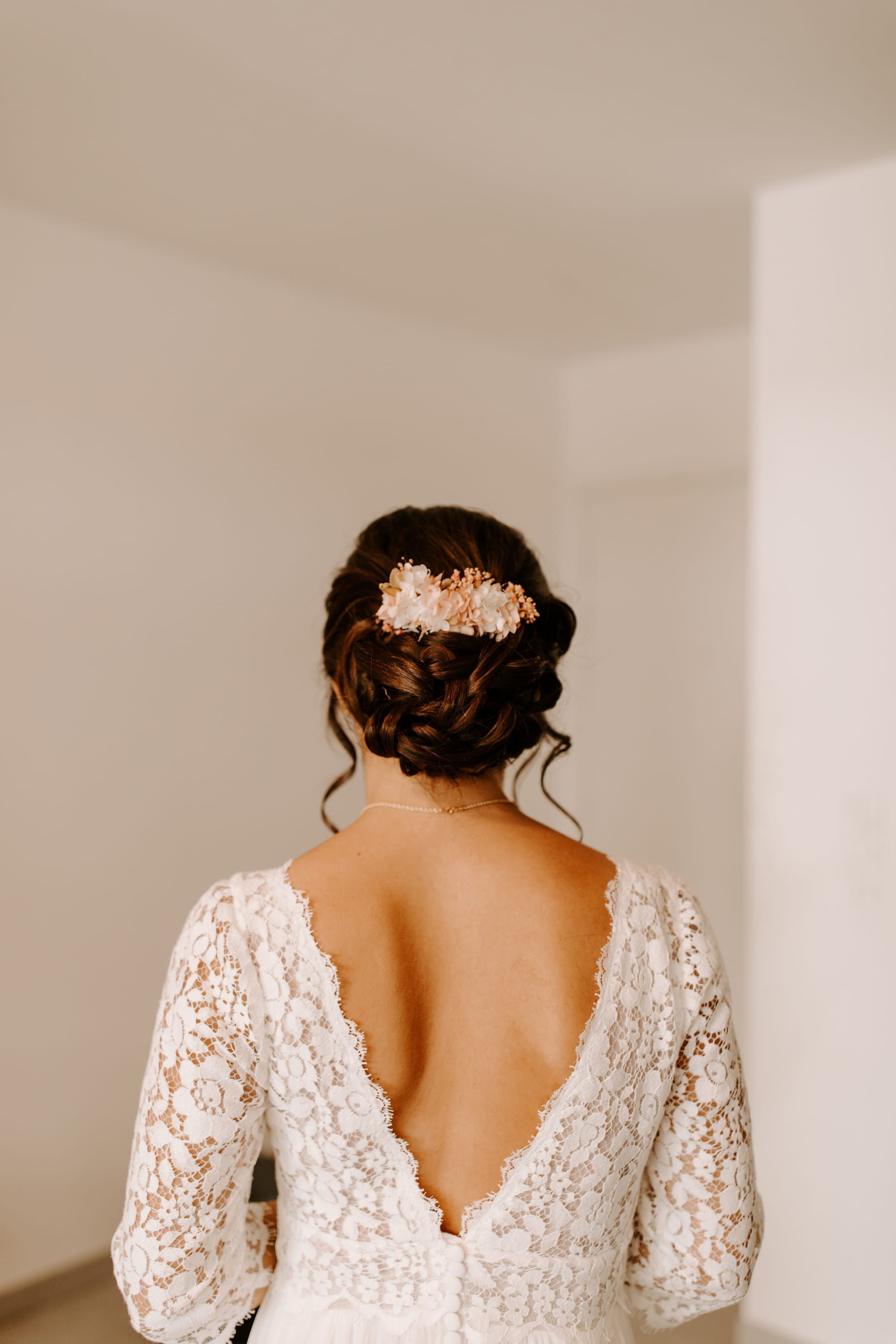 Chignon bas de mariée travaillé d'une base boucle avec demi- couronne de fleurs roses et blanche