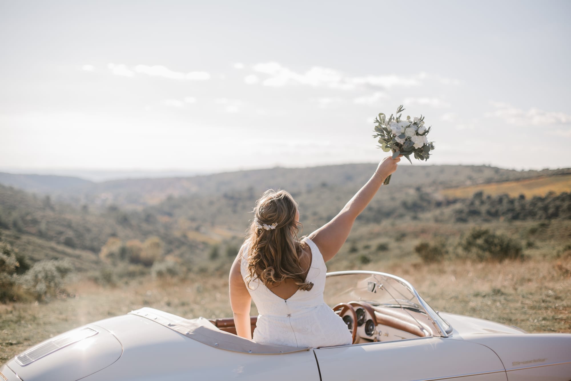 Mariée en voiture décapotable qui lance son bouquet de mariée