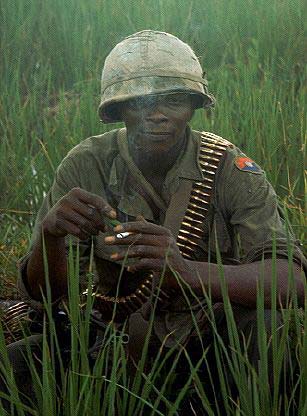 Vietnam War An American 9th Division machine gunner swathed in bullet belts, smokes a cigarette, 1968