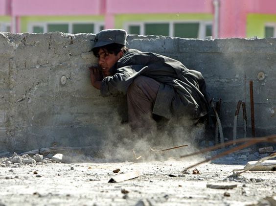 Afghanistan War May 12, 2005, An Afghan policeman takes cover as protesters throw stones in Logar province, about 25 miles southwest of Kabul.