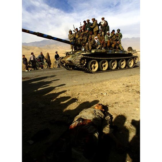 AfghanWar November 13, 2001, Northern Alliance fighters ride on a T-62 tank past a dead Taliban fighter on the motorway 3km north of Kabul